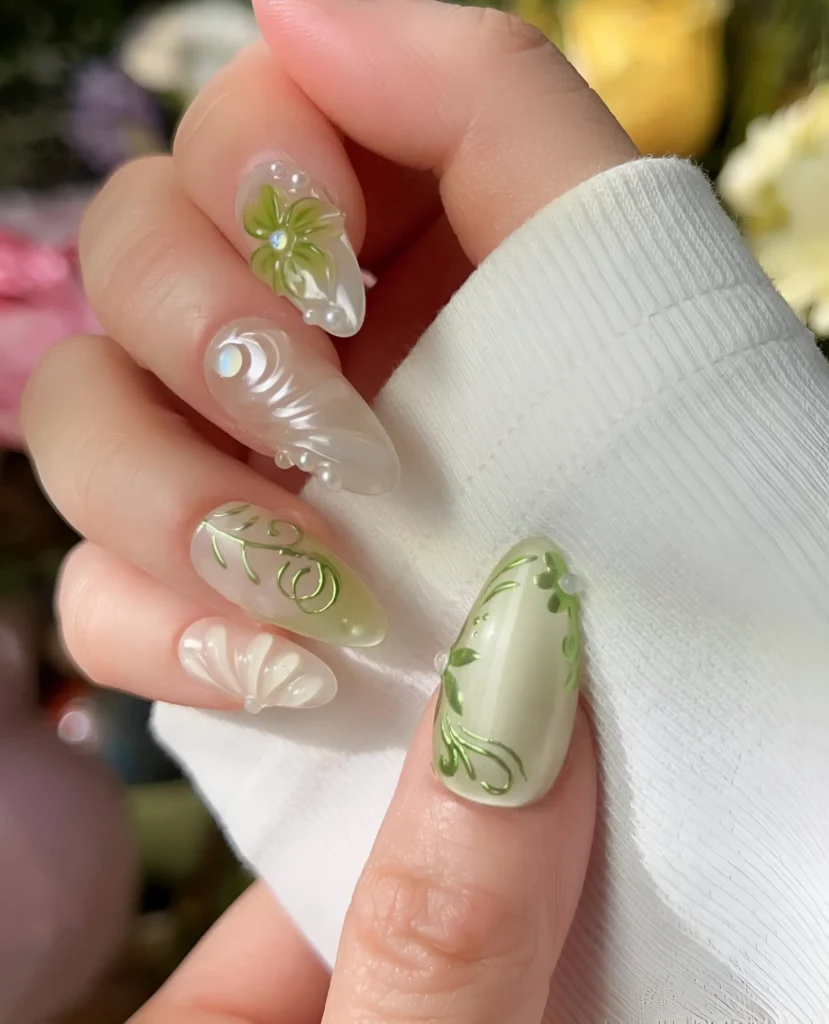 Almond nails mixing painted green botanical vines, 3D green flowers, white sculpted textures/swirls, and pearlescent bases.