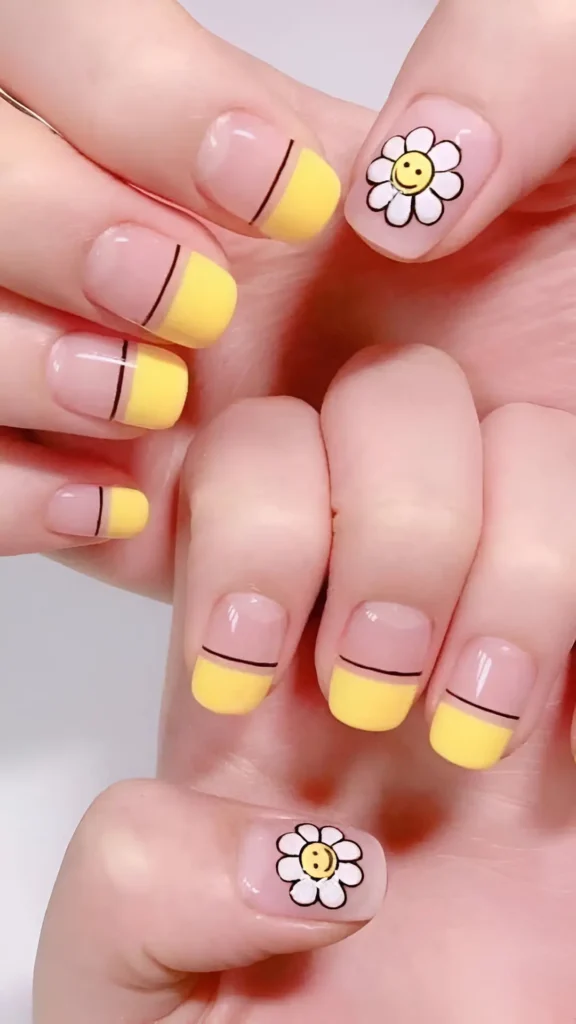 Short square nails mixing pastel yellow French tips defined by a thin black line, and sheer nails with outlined white daisies having yellow smiley centers.