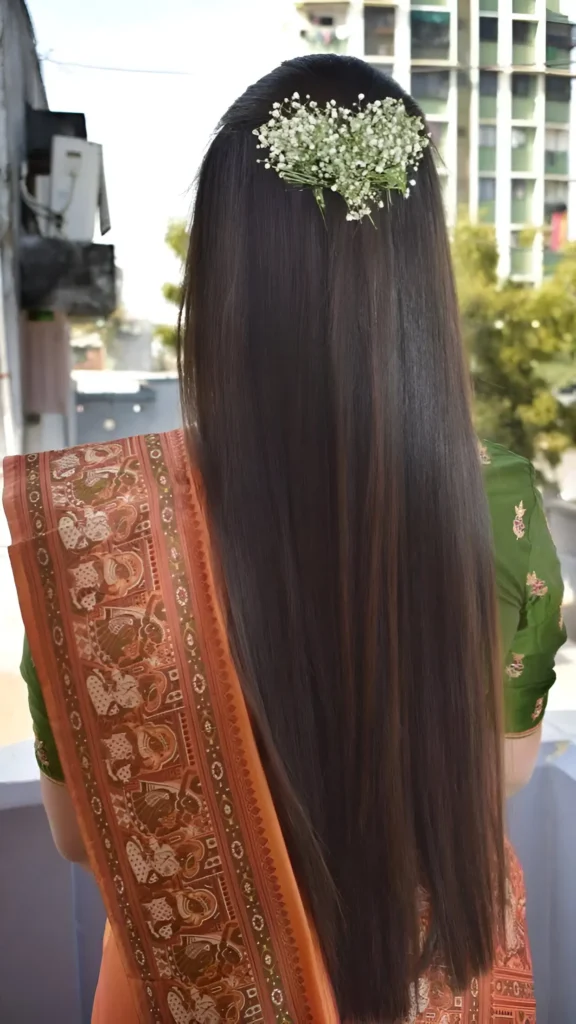 Back view of very long straight dark hair adorned with a horizontal cluster of baby's breath flowers.
