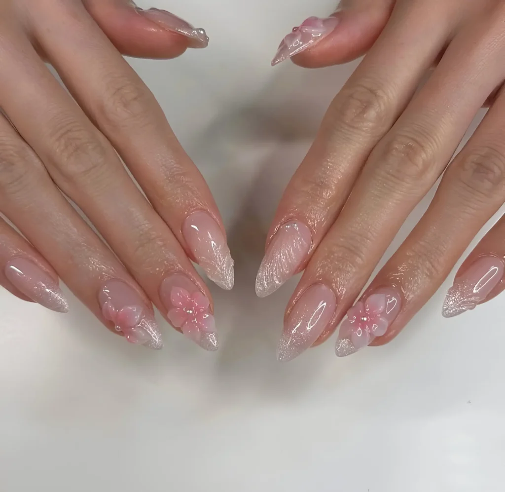 Long almond nails with sheer nude base, sparkling silver glitter gradient tips, and delicate pink 3D floral accents.