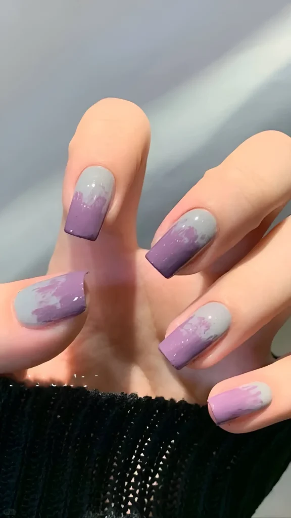 Square nails with abstract smudged gradient effect using dusty purple and light grey polish.