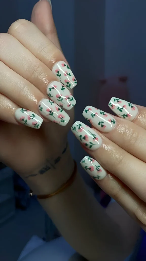 Coffin-shaped nails with a milky white base covered in an all-over ditsy floral pattern featuring tiny pink buds and green leaves.