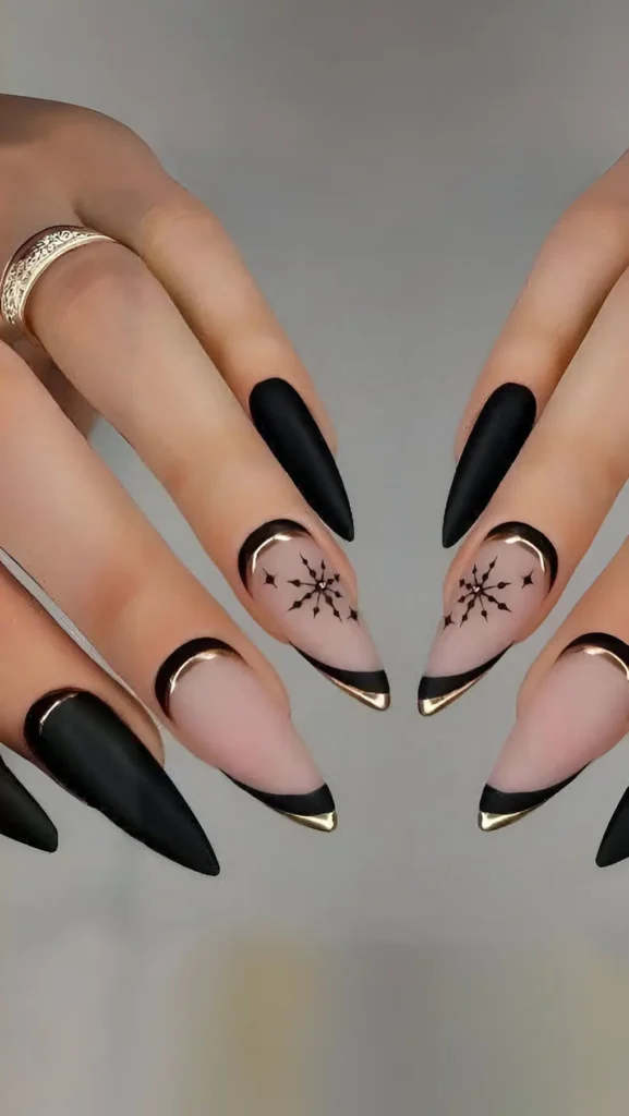 Long stiletto nails with mixed design: matte black nails and sheer nails with black V-tips outlined in gold, featuring black snowflake graphics.