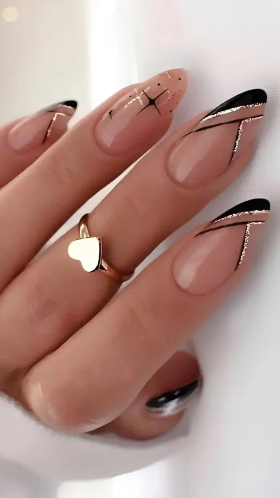 Long almond nails with sheer base featuring abstract black angled designs outlined with gold glitter, plus a star graphic accent nail.