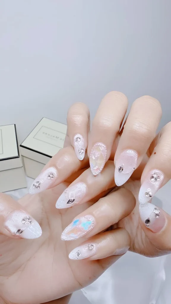 Extravagant 'frosted fantasy' nail art with textured white base, iridescent flakes, large crystal clusters, and metallic details.