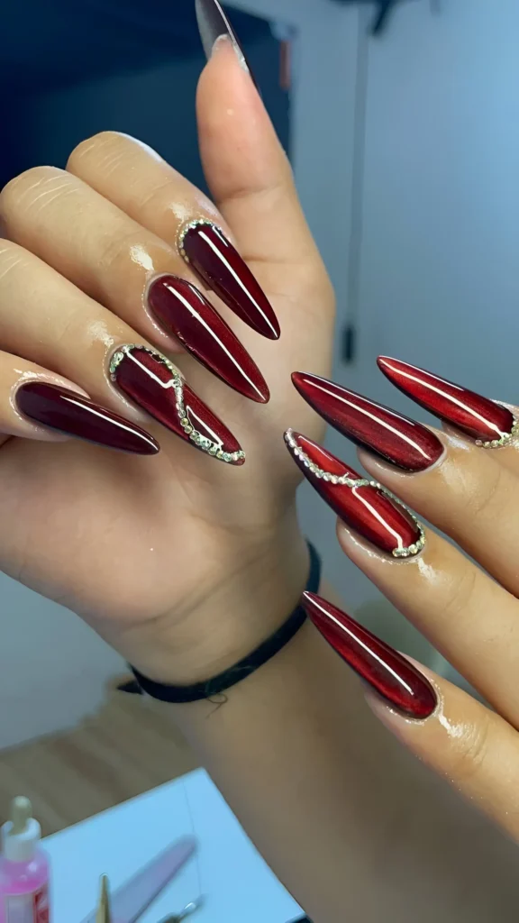 Long stiletto nails with a deep oxblood red cat-eye effect base, accented with sweeps of chunky silver glitter paste along the sides.
