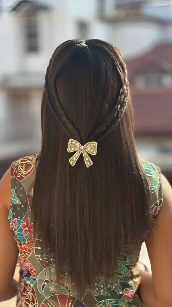Back view of long straight dark hair in a half-up style with two braids forming a V-shape, accented by a sparkly bow barrette.