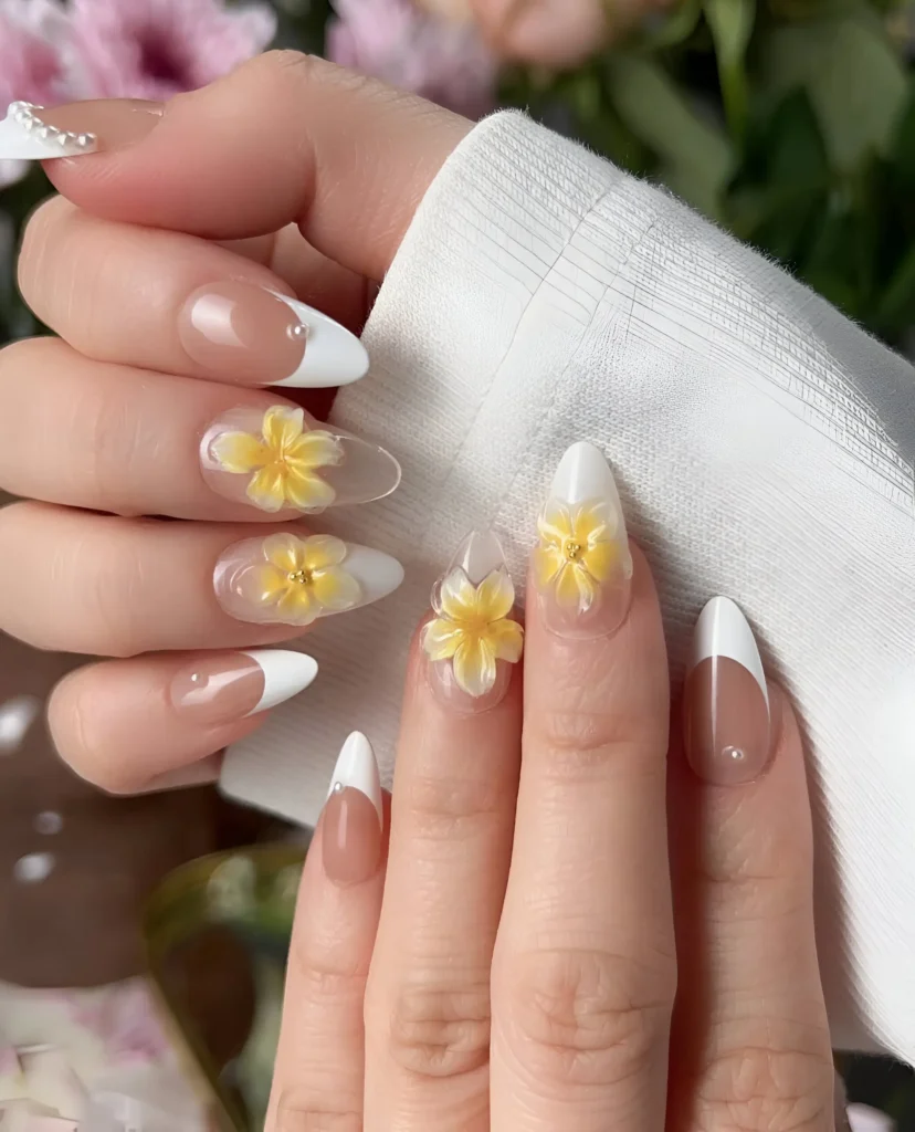 Almond nails mixing classic white French tips on a sheer base with sunny yellow 3D flower accents with gold bead centers.