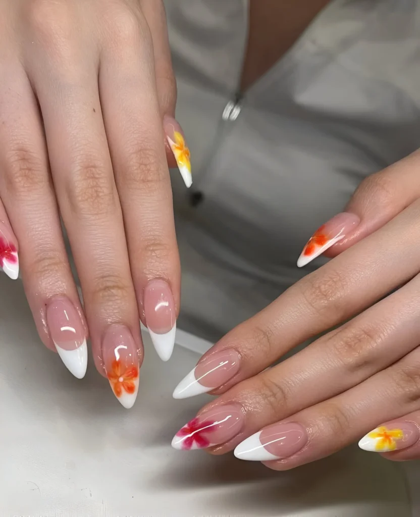 Almond nails mixing classic white French tips with tips featuring painted watercolor-style flowers in orange, yellow, and red.