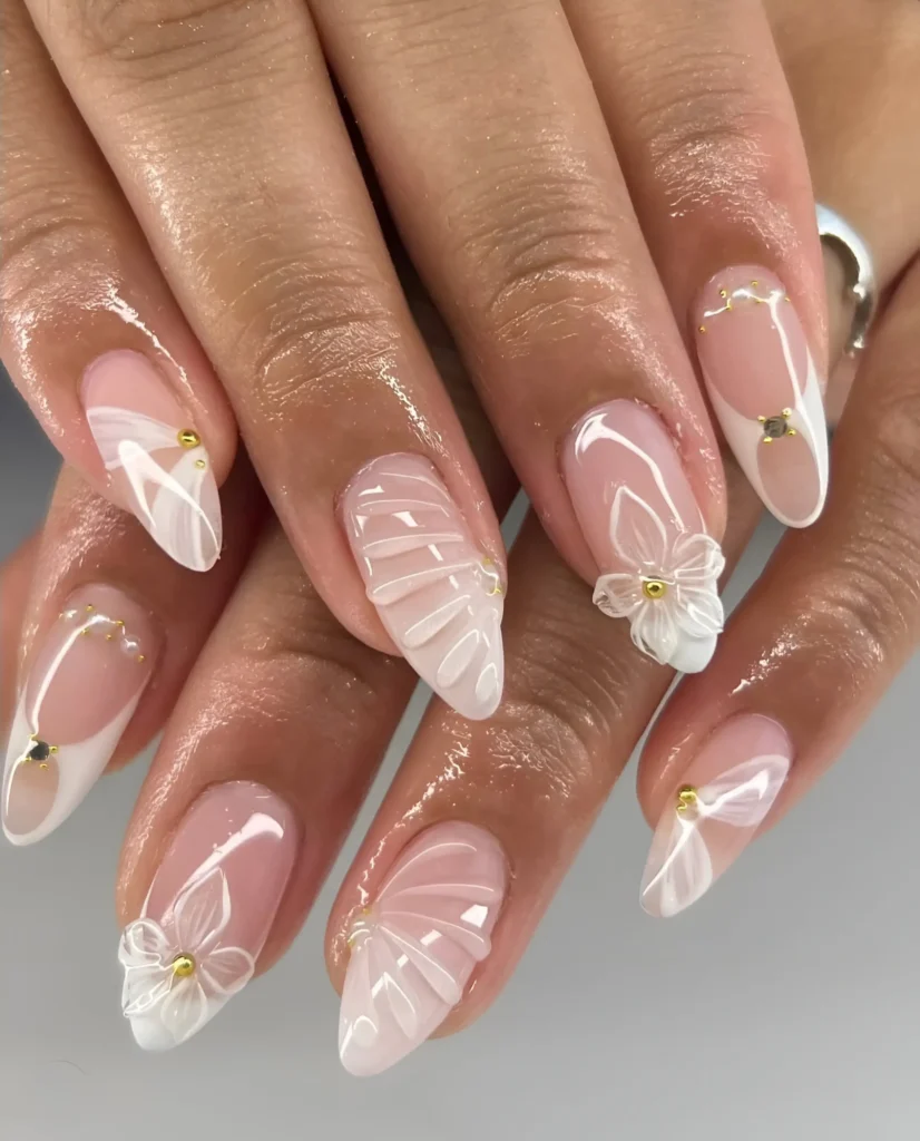 Almond nails with sheer base featuring intricate white 3D textures (fans, drapes), white 3D flowers, subtle white French elements, and gold stud accents.