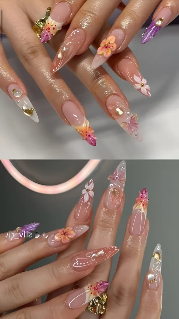 Long stiletto summer nails with sheer base, ornate multi-color 3D flowers near tips, clear water droplet accents, and pearls.