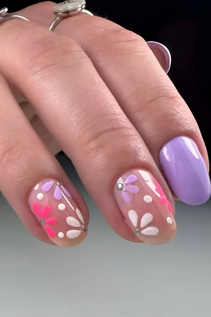 Short rounded nails with solid pastel lilac and sheer nails with pink and white flower nail art.
