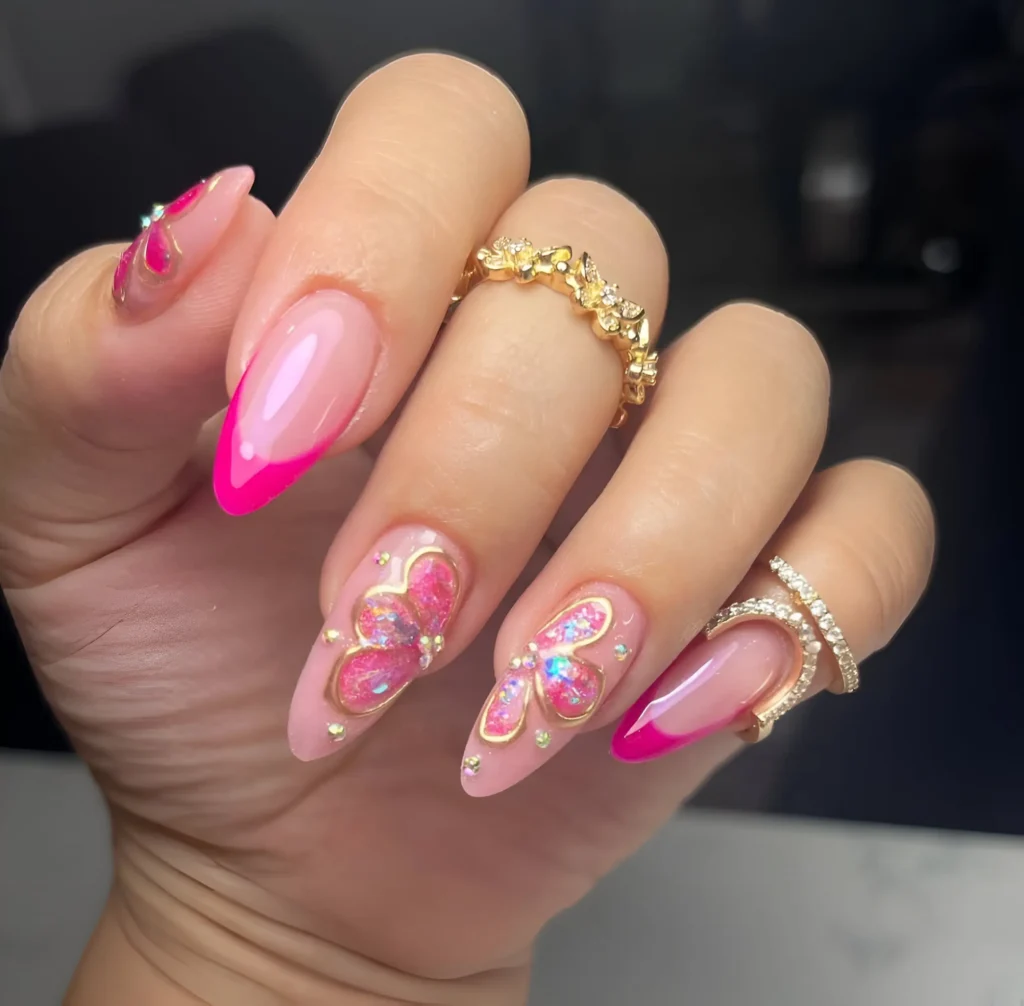 Almond nails with light pink base mixing hot pink V-French tips and large glitter butterflies outlined in gold with gem accents.