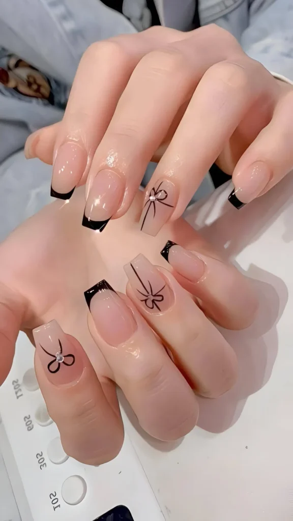 Square nails with mixed design: classic black French tips and sheer nails decorated with a black outline bow motif accented with a rhinestone.