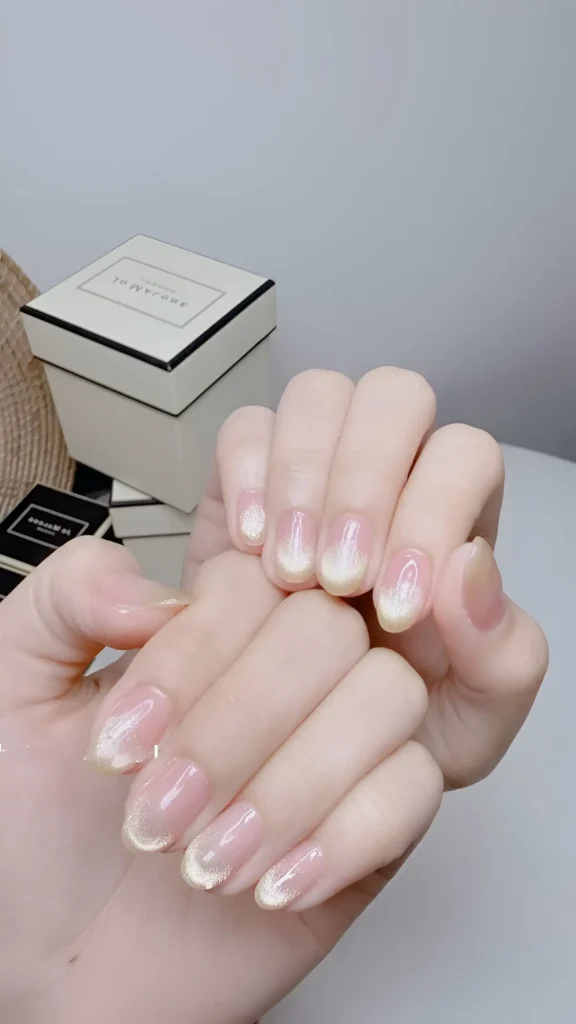 Subtle aura nails: rounded shape with sheer base, soft diffused yellow/gold center glow, and delicate gold glitter tips.