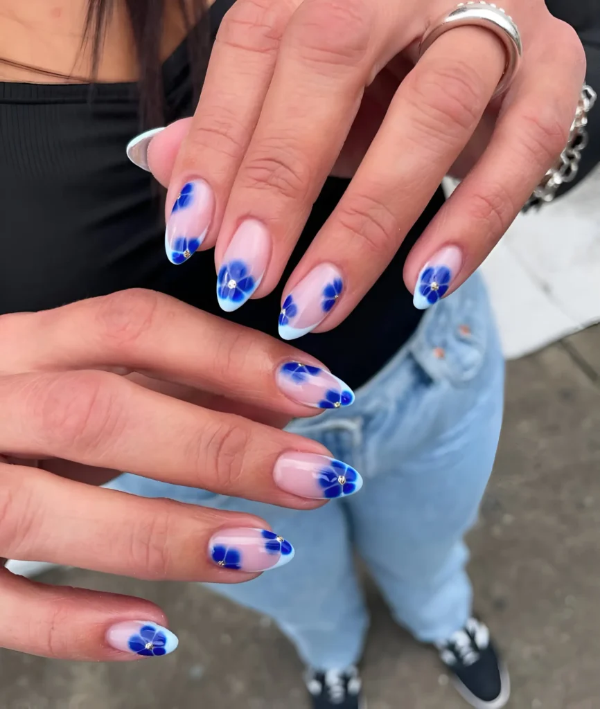 Pretty French manicure with white tips, sheer base, and vibrant blue painted florals centered with gems.