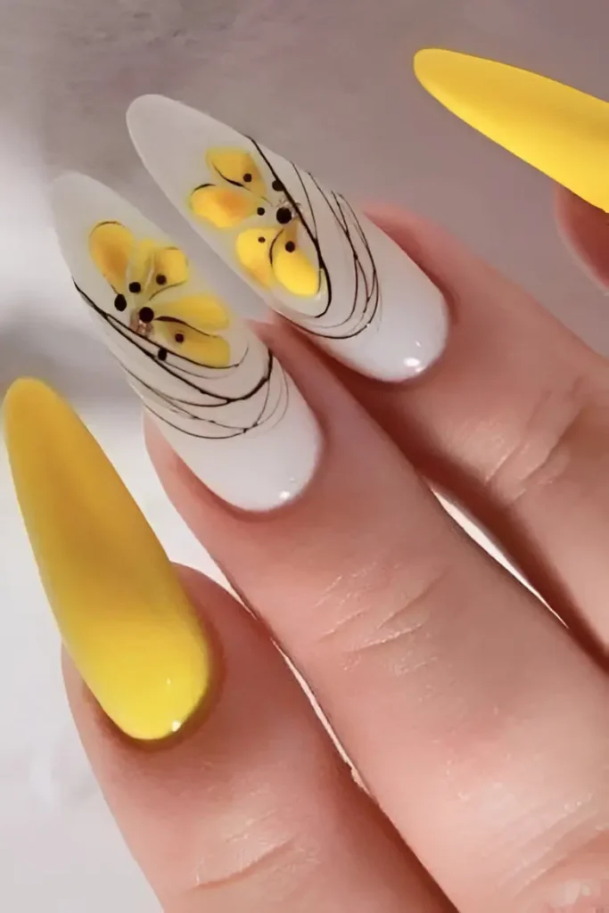 Long almond nails mixing solid bright yellow polish and milky white nails painted with abstract yellow floral/wing shapes with black dots, overlaid with thin black swirl lines.