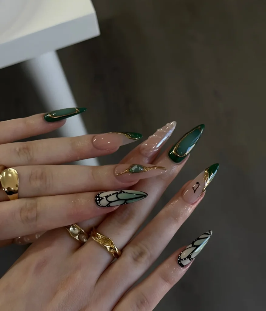 Elegant stiletto nails showcasing green and gold butterfly wing art paired with deep green nails and gold lines.