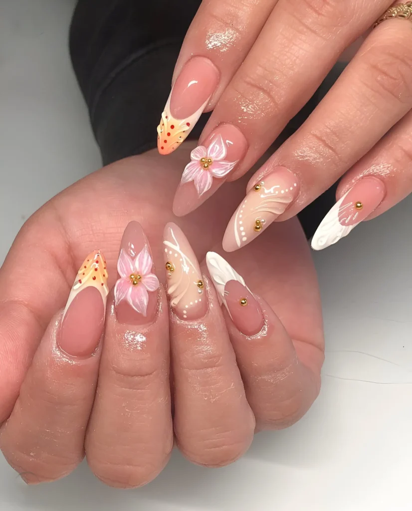 Almond nails mixing white tips with yellow/orange painted details, white sculpted textures, pink 3D flowers, and gold stud accents on a sheer base.