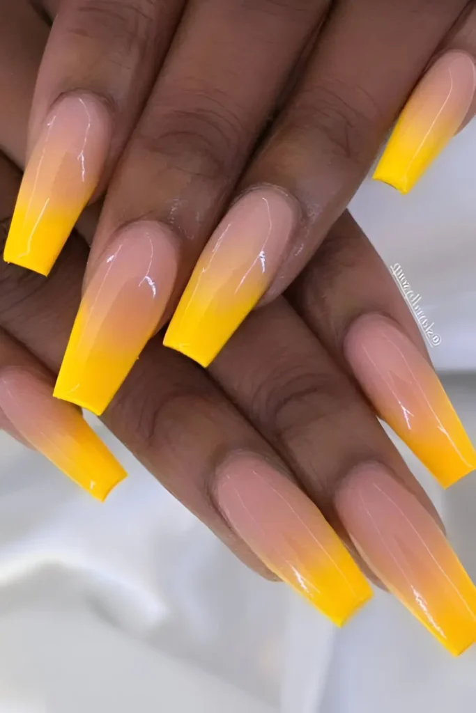 Long coffin-shaped nails with a smooth ombré effect, fading from bright yellow at the tips to a sheer nude/pink base near the cuticles.