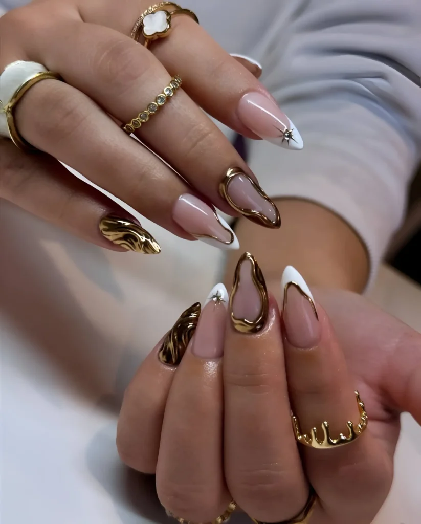 High-contrast stiletto nails pairing crisp white V-French tips with sculptural molten gold accents and starbursts.