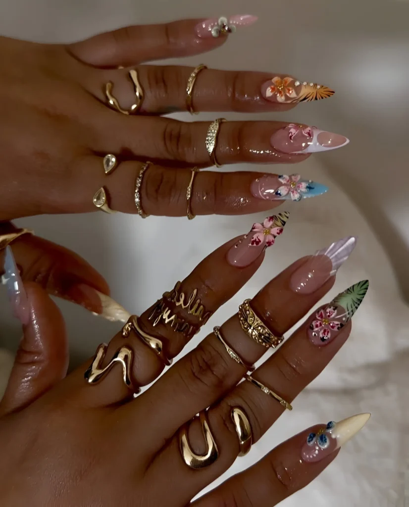 Artistic stiletto nails with mixed-media florals (orchids/lilies) using detailed painting and 3D sculpting.