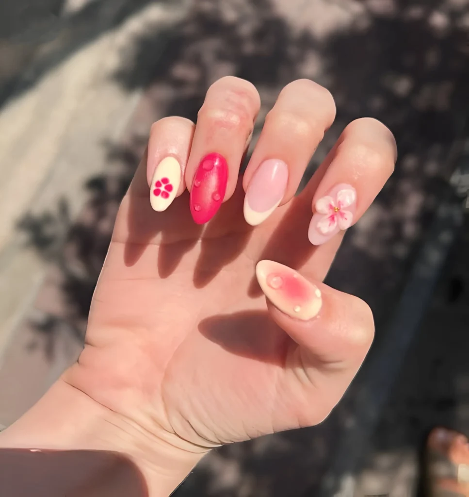 Almond nails mixing white French tip, painted floral, 3D flower, pink aura nail, and solid coral nail with 3D droplet.