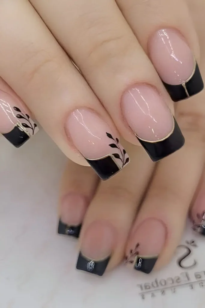 Square nails with sheer base featuring black French tips outlined in gold, with black botanical illustrations extending from the tips.