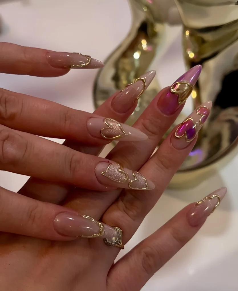 Glamorous stiletto nails featuring sculptural gold heart outlines contrasted with metallic pink and textured glitter accents.