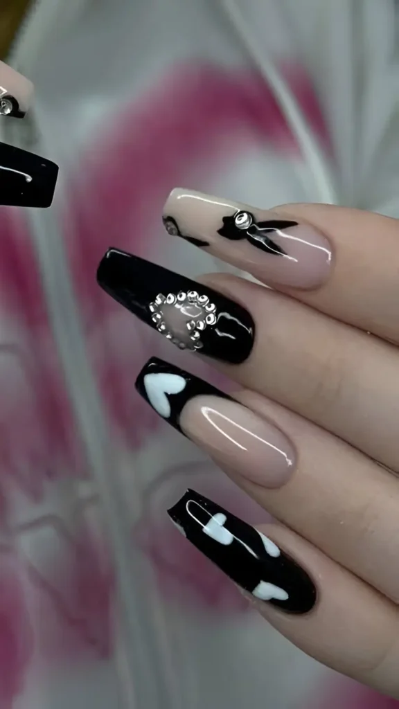 Long coffin nails with a mixed black and sheer design featuring white hearts, a black bow, and a rhinestone heart cutout accent.