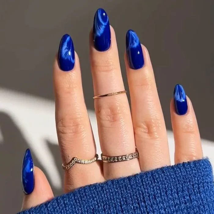 Long, almond-shaped nails with a blue and white marble nail art design.
