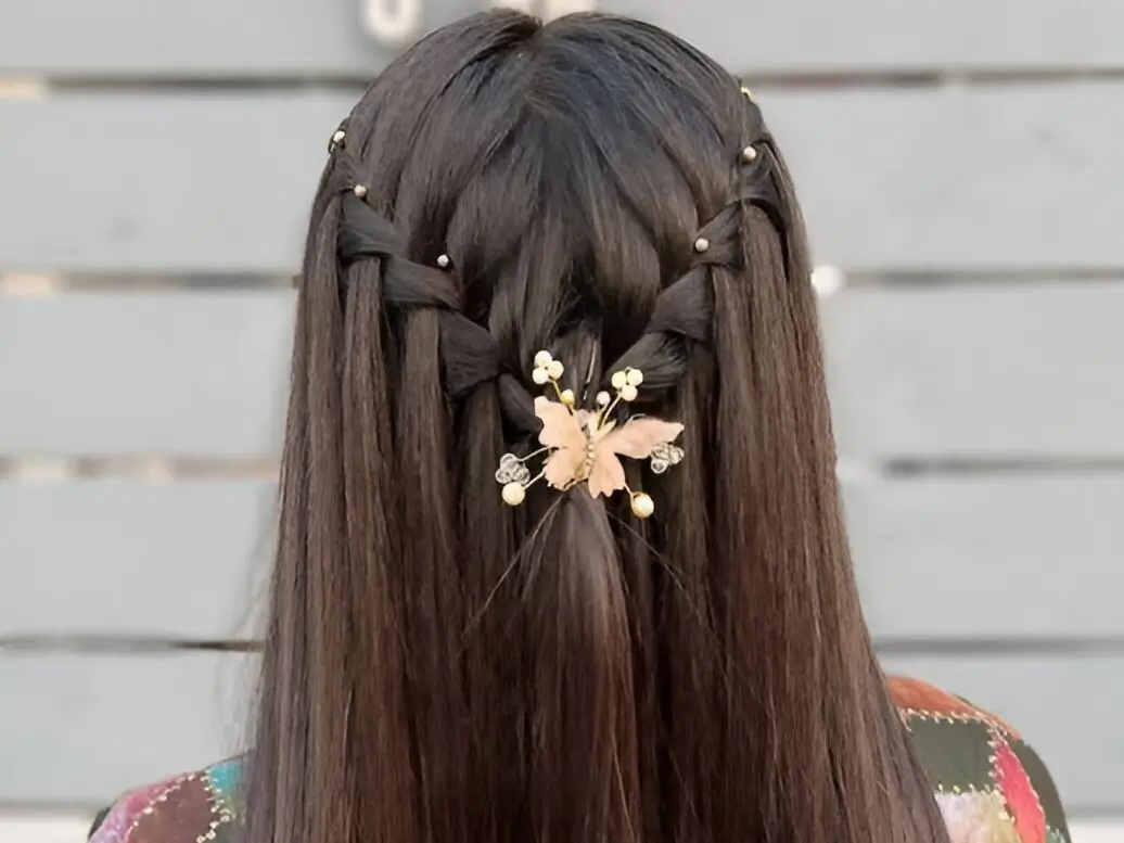 Half-up braided hairstyles for long hair featuring bead-accented braids meeting under a gold butterfly clip on dark hair.