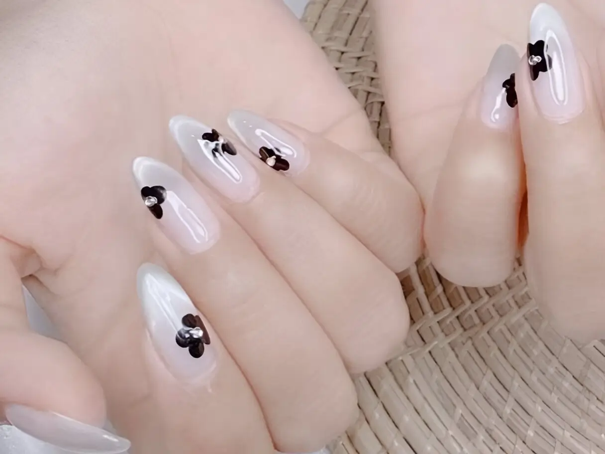 Classy nail ideas 2025: minimalist black flower art on milky white almond nails.