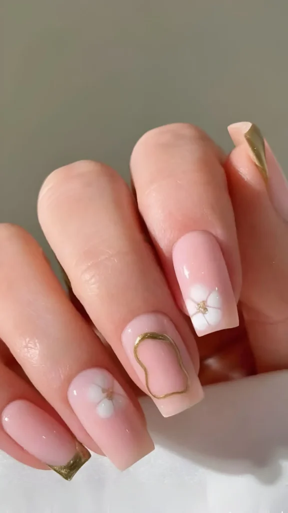 Cute soft pink nail design with abstract gold metallic accents, white flowers, and gold frame detail.