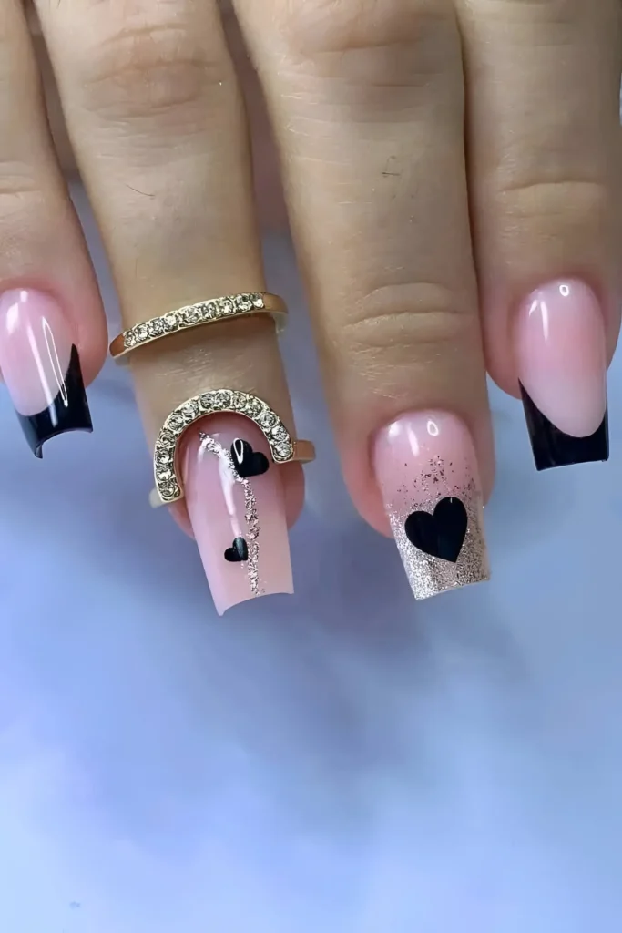 Cute pink base nail design with black angular French tips, black hearts, and champagne glitter accents.