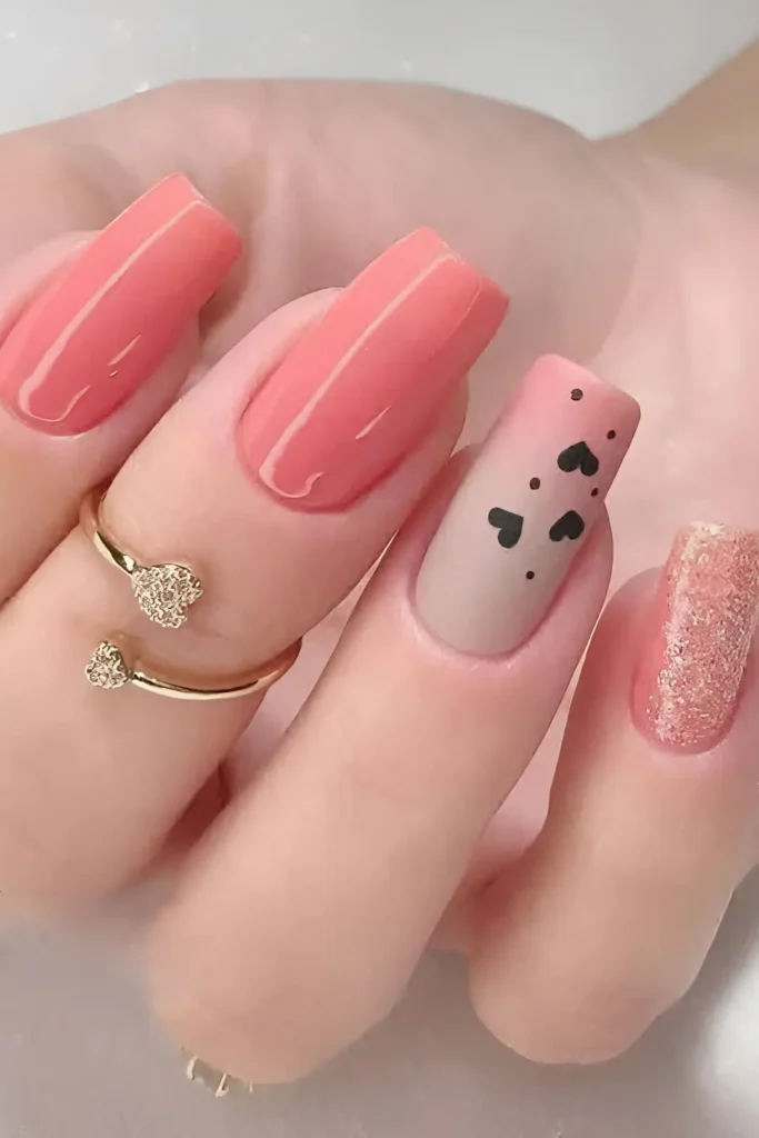 Cute coral pink nail design mixing glossy, matte nude with black hearts, and textured glitter nails.