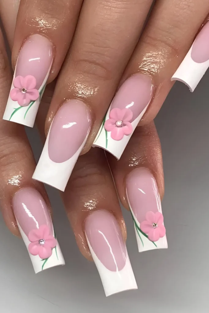 Cute pink French manicure design with white tips and 3D pink flowers with rhinestone centers.