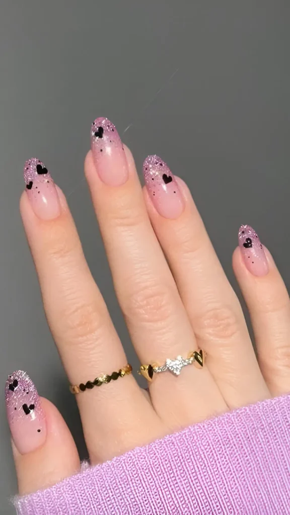 Cute pink glitter ombre nail design with small black heart accents scattered on tips.