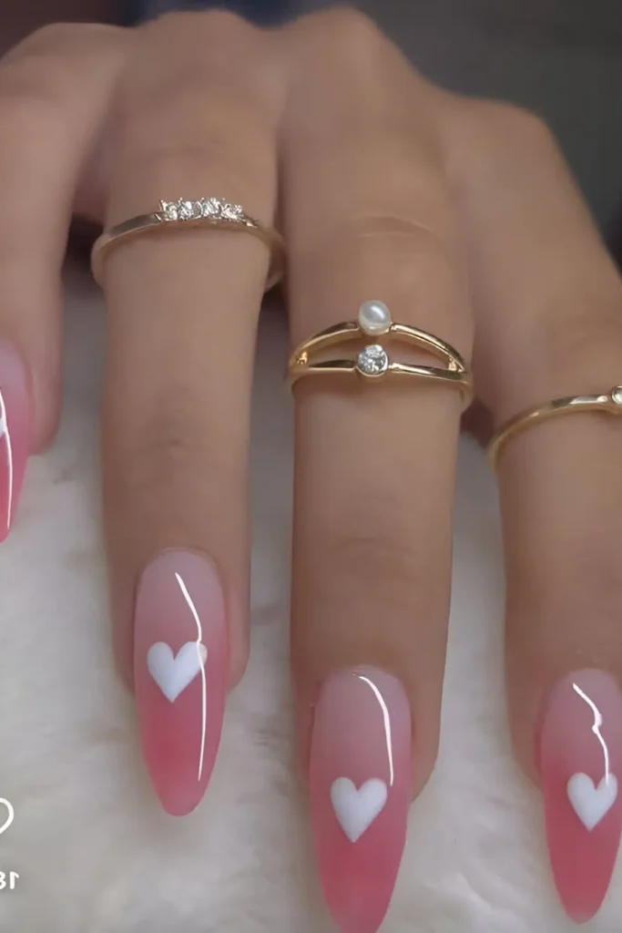 Cute pink gradient ombre nail design with white heart accents on almond nails.