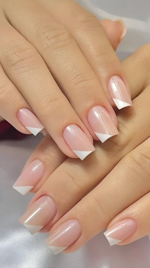 Modern French manicure nail design with sheer pink base and angled white tips.