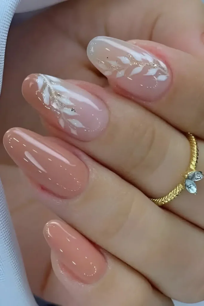 Cute peachy pink nail design with white painted leaf sprigs dusted with gold glitter.