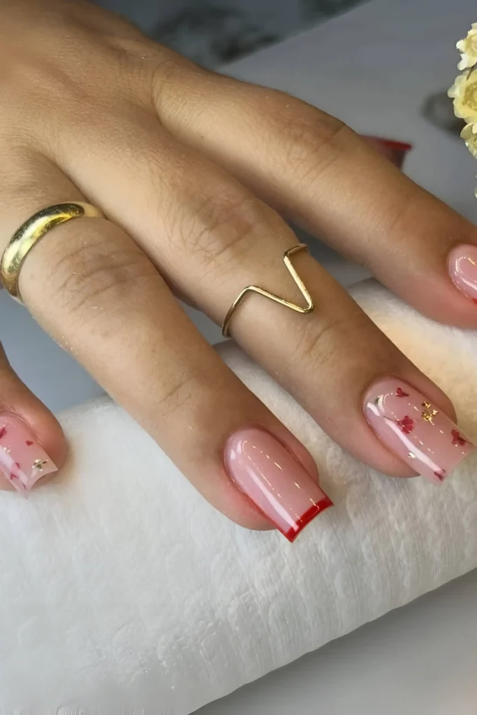 Cute pink sheer base nail design with tiny red hearts, gold flakes, and red micro French tip.