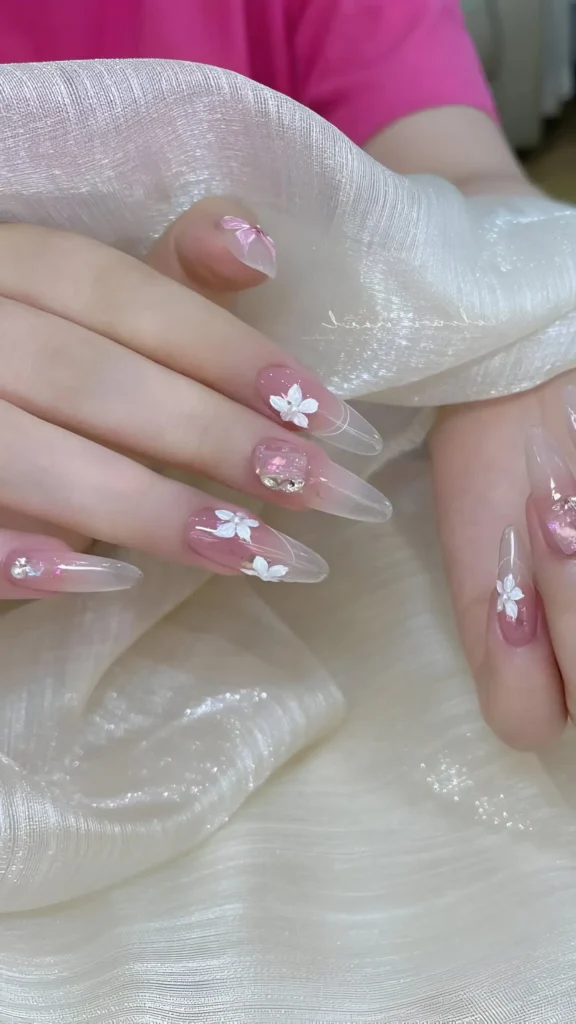 Cute sheer stiletto nail design with white painted flowers and clear rhinestone clusters.
