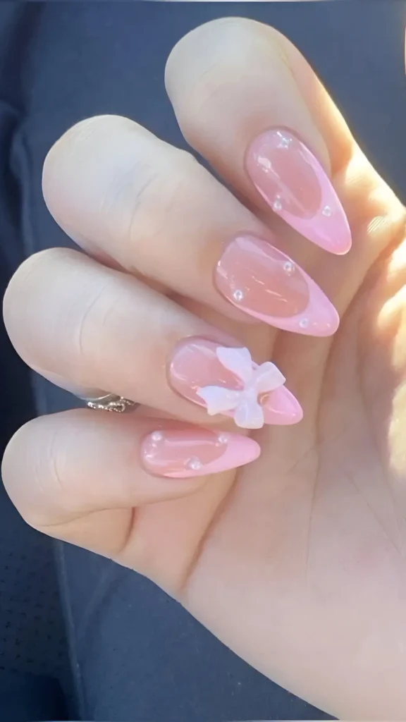 Cute pink sweetheart French tip nail design with 3D white bow and pearl accents.