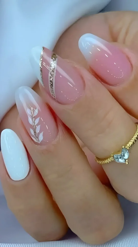 Cute pink and white nail design with ombre tips, botanical sprig, and gold glitter accents.