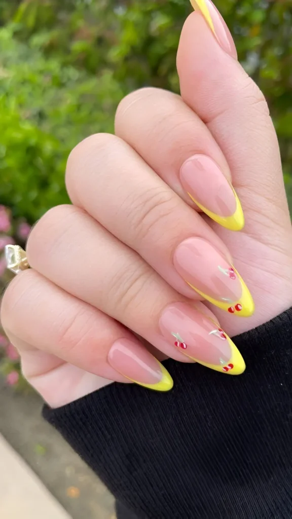 Cute French manicure on almond nails with bright yellow tips and tiny cherry accents.