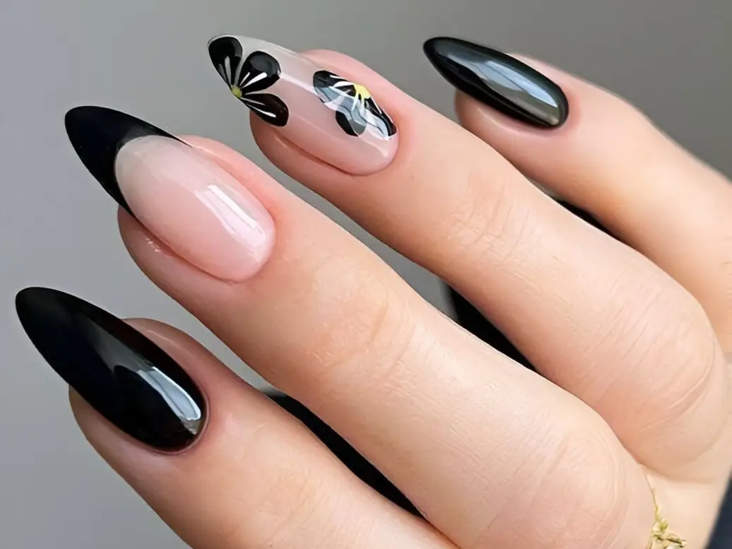 Close-up of gorgeous black nail designs on long almond nails, featuring solid black, black French tips, and black floral art on a sheer base.