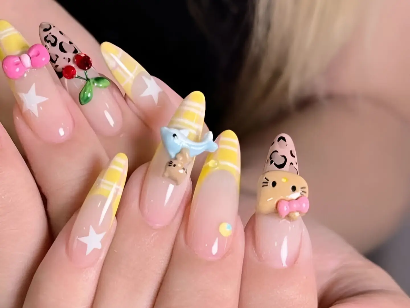Detailed example of yellow nail ideas: Long pointed nails feature pastel yellow French tips over a sheer base, adorned with maximalist 3D charms (bow, bird, cat), plus painted stars, roses, and leopard print.