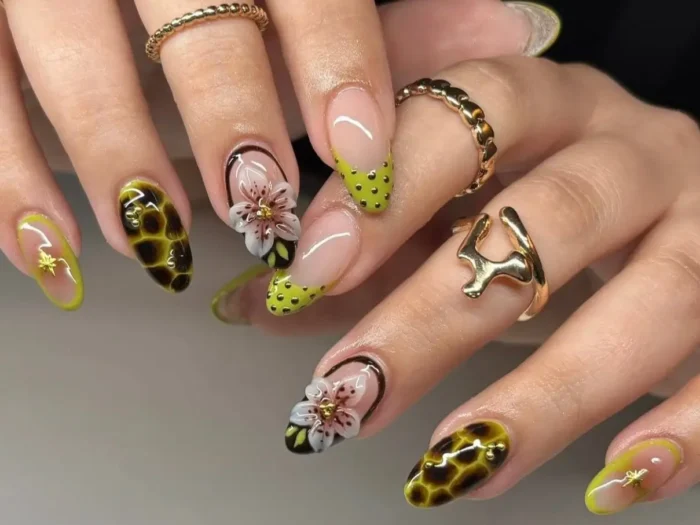A close-up of a manicure showing a mix of trending nail designs for 2025, including tortoiseshell patterns, green French tips, and 3D floral accents.