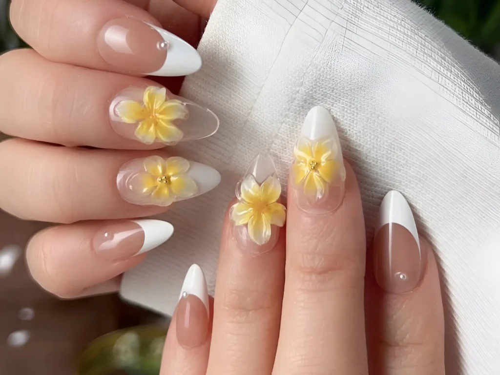 Close up of trendy almond nails featuring white French tips and accent nails with 3D yellow flowers with gold centers.